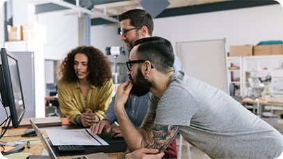 Three people standing by a desk working on a desktop computer.