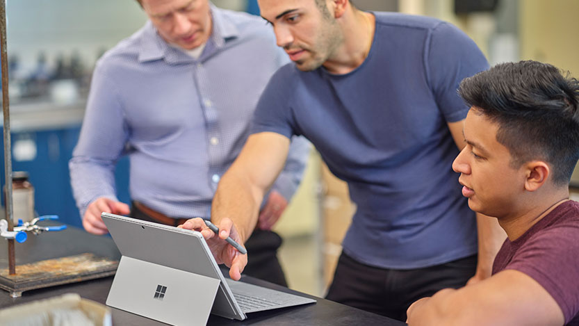 One person points at a laptop computer screen while two more people pay attention.