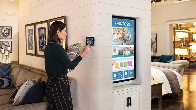 A woman interacts with a tablet attached to the wall of a furniture store.