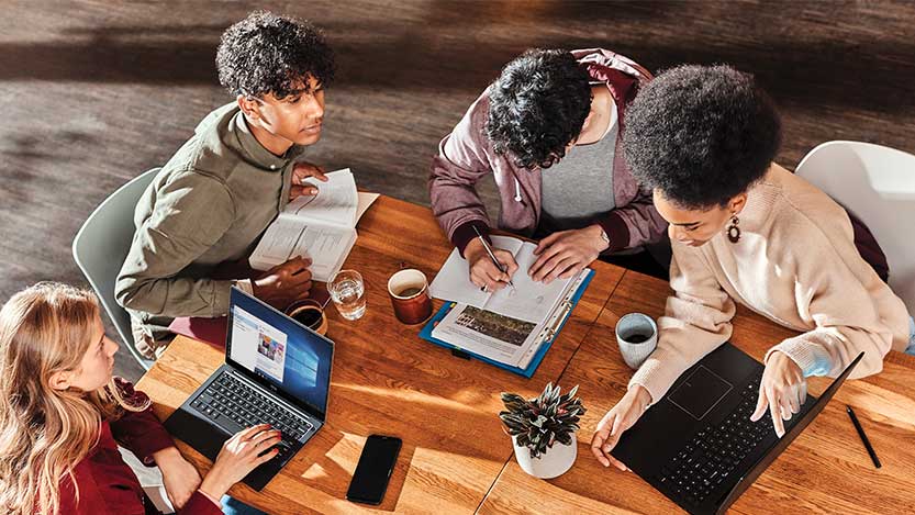 Four young people sit around a table with laptop computers and books.