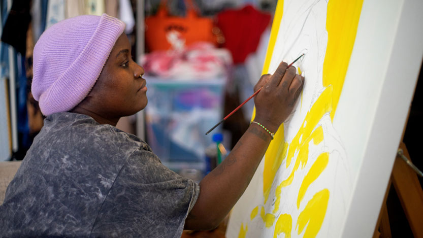 A woman indoors painting on a canvas.