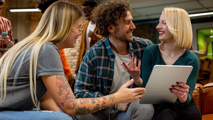 Three people sitting on a couch smile while looking at each other.