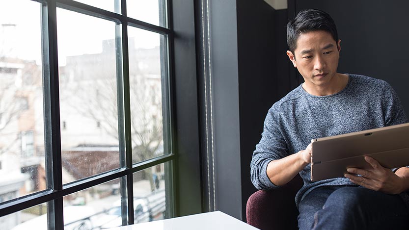 A man sitting by a window works on a tablet.