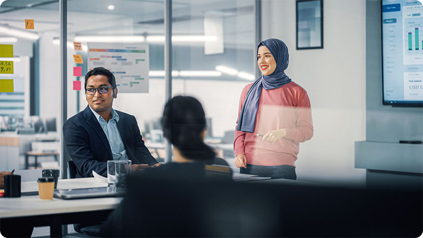 Three coworkers talking and smiling in a conference room at work.