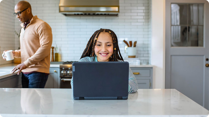 Child sitting at a kitchen couter with a laptop. A person is walking by in the background.