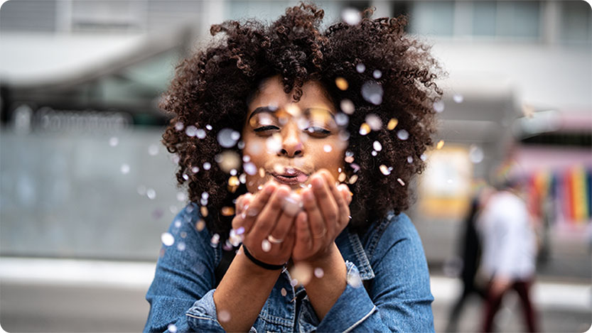 A person facing the camera and blowing confetti to it.