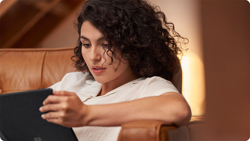 A person laying on a coutch using a tablet.